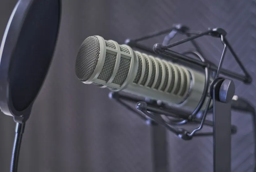 A close-up of a professional studio microphone with a pop filter, set against a soundproof, padded background, ready for recording audio or podcasting.